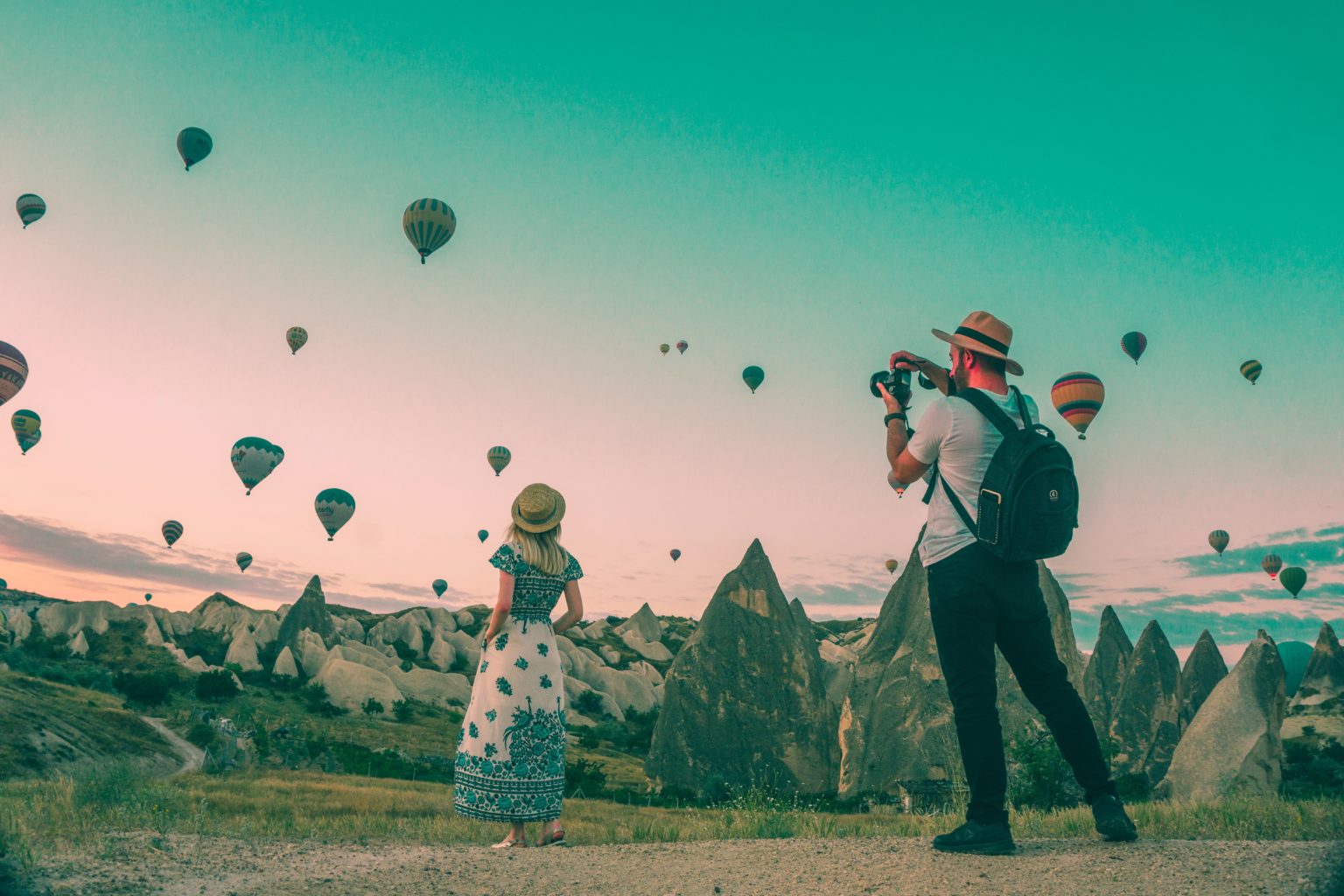 two people taking pictures outside with several hot air balloons in the sky